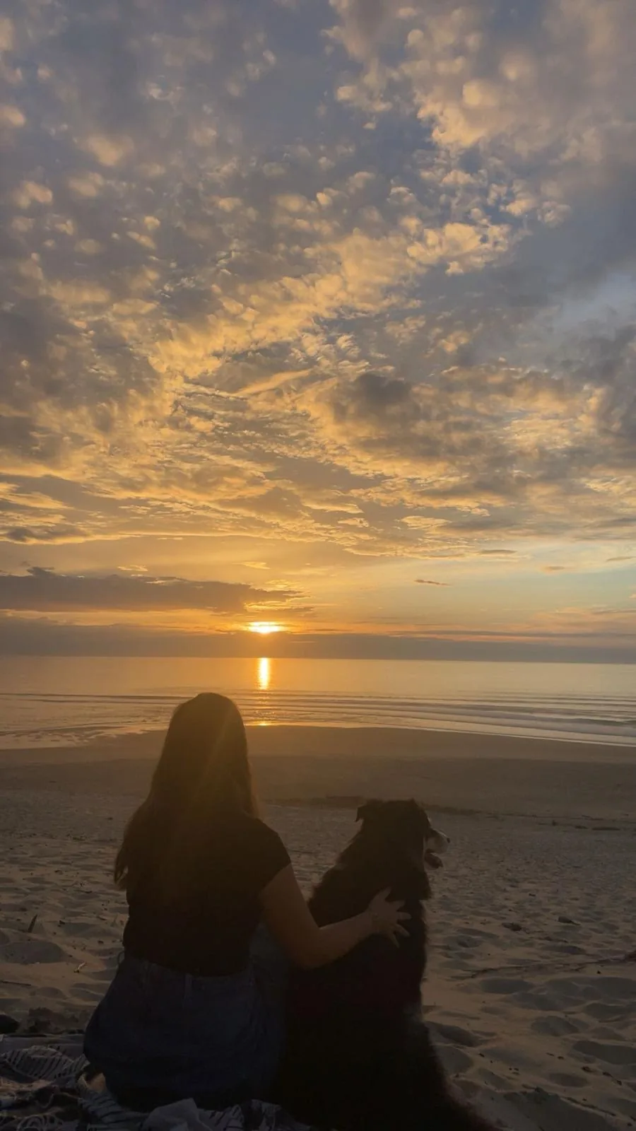 Élodie Dubos assise sur la plage avec son chien, face au soleil couchant sur la mer